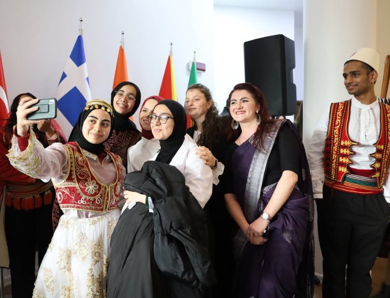 Students in traditional costumes take a group selfie in front of national flags at WBU